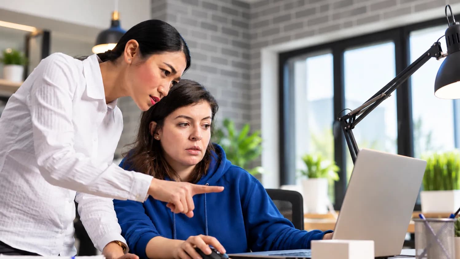 Technical lead pointing out a detail to a colleague working at a laptop